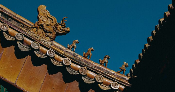 Fotografia em cores de detalhe de um telhado no Museu do Palácio em Pequim. Vê-se uma fileira de pequenas esculturas, sendo um dragão e, à sua frente, quatro criaturas menores.