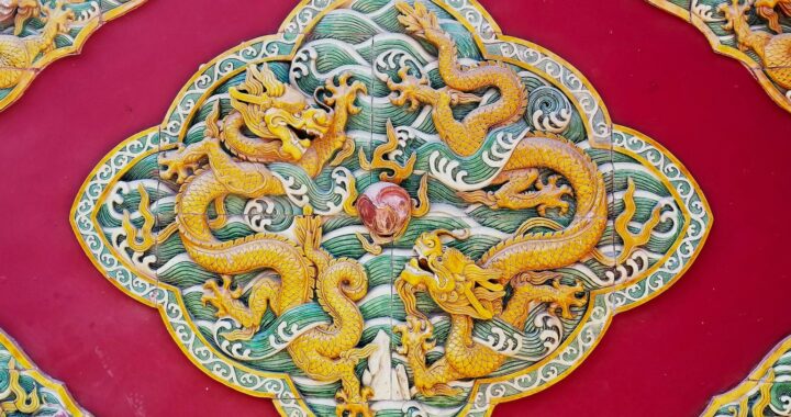 Fotografia em cores de detalhe da decoração em templo no Beihai Park, mostrando dois dragões dourados ao redor de uma pedra vermelha.