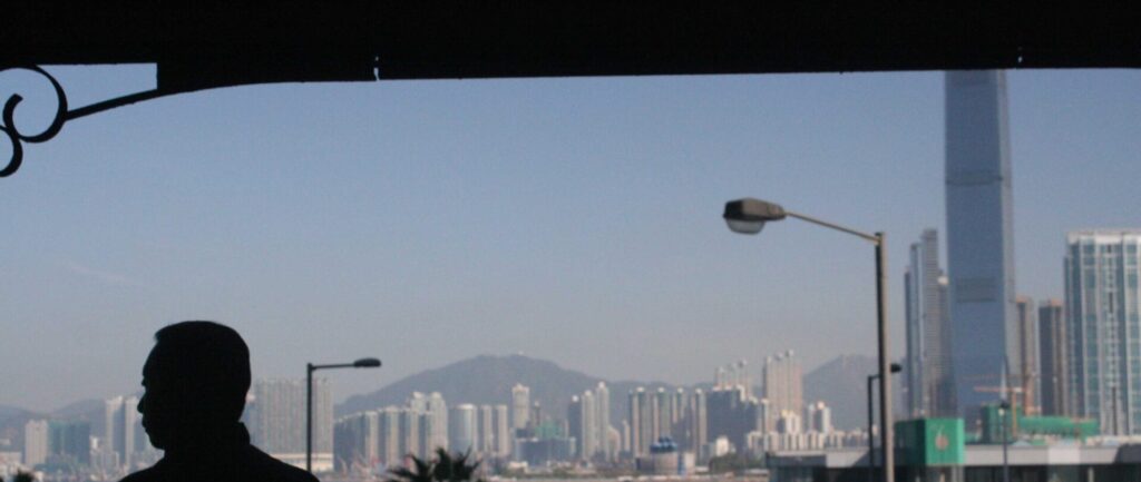 Foto da skyline de Hong Kong, em que a silhueta de um homem está em primeiro plano e ele olha para o lado.