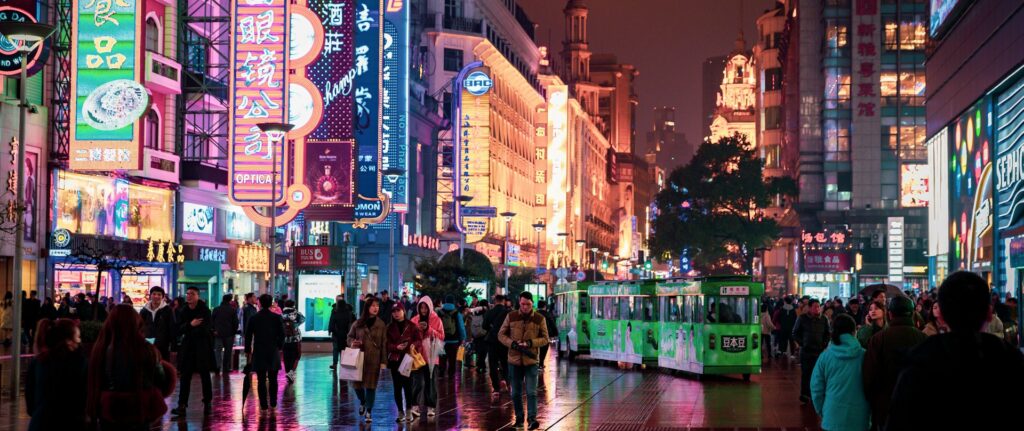 Fotografia em cores de uma rua de Macau à noite com pedestres fazendo compras em meio a luminosos coloridos.