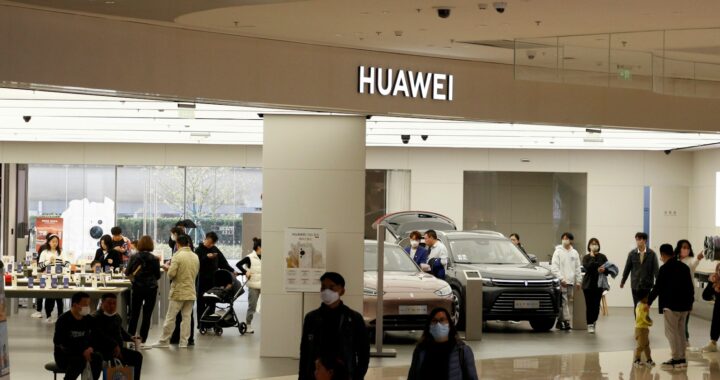 Um grupo de pessoas em um prédio amplo, com uma loja da Huawei ao fundo vendendo carros