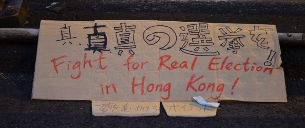 Placa escrita em mandarim e em inglês com a mensagem de lute por eleições democráticas em Hong Kong